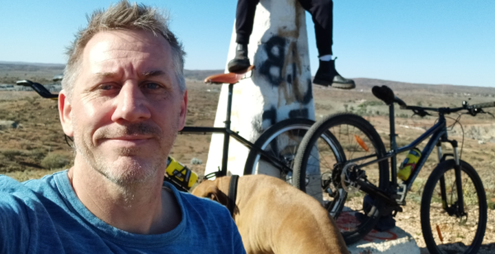 Ruben in foreground with bicycles, a dog and Harlz's legs astride the triangulation point on Round/Red Hill behind him.