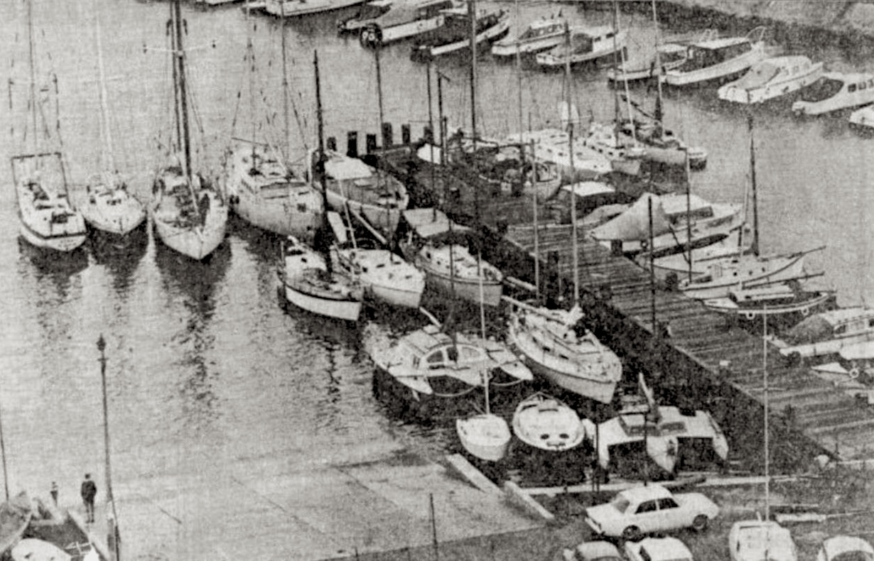 A black and white photo of jetty with a dozen or so yachts moored alongside